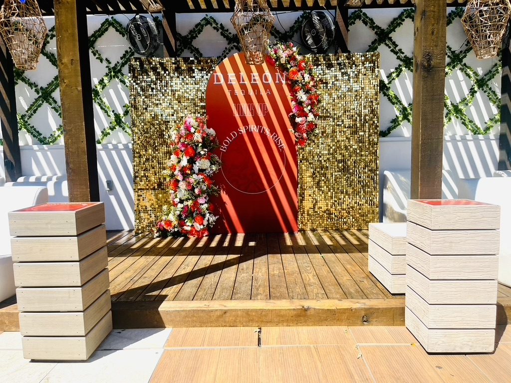 DeLeón Tequila photo backdrop with gold sequin walls and floral arrangements