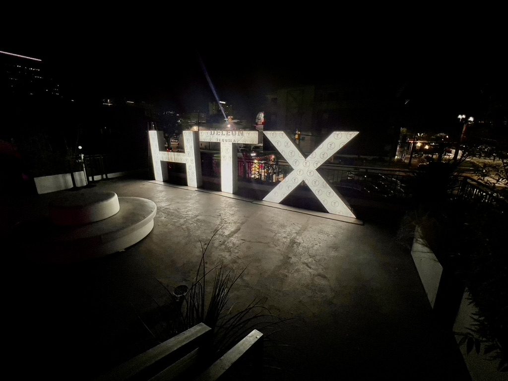 Illuminated HTX letters with DeLeón branding at night