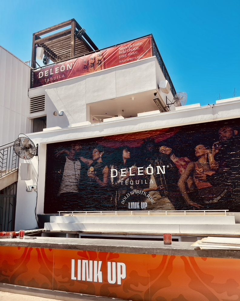 Venue exterior with a DeLeón Tequila rooftop banner, wall mural, and a Link Up branded bar front