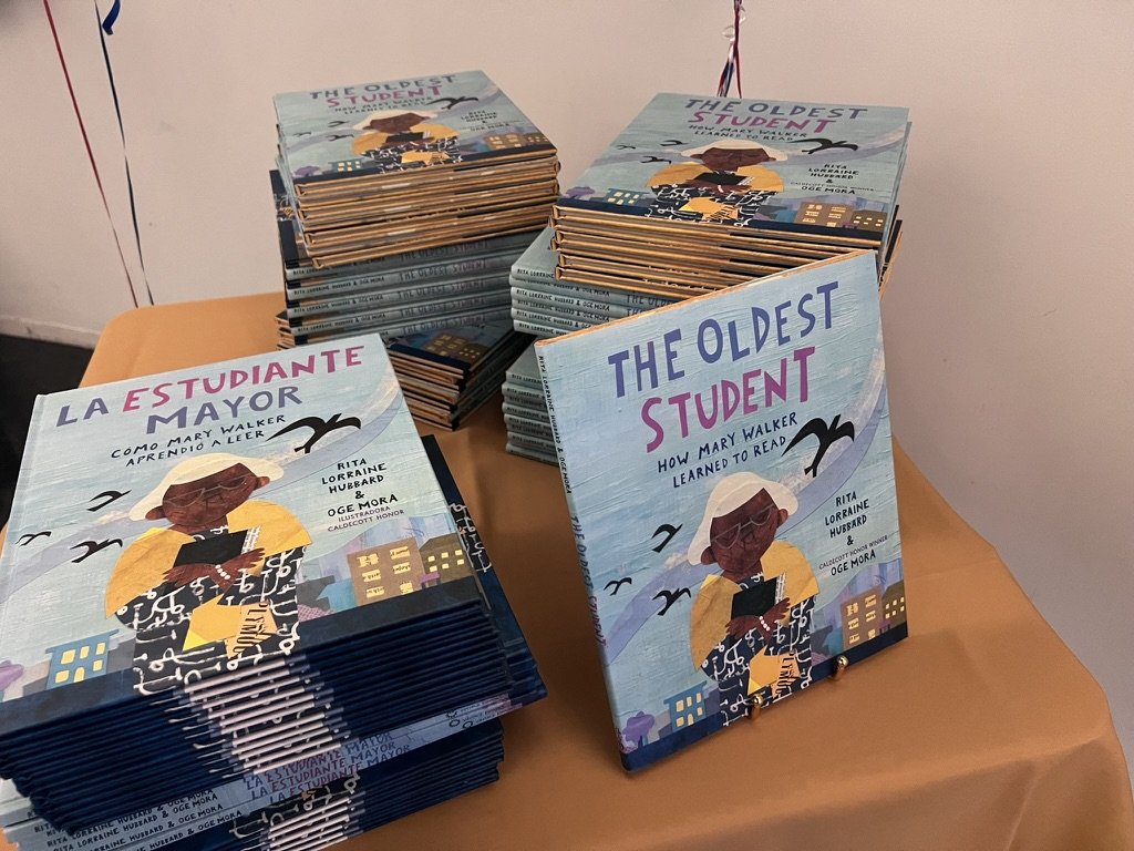 Stacks of The Oldest Student and La Estudiante Mayor picture books set out on a table for families