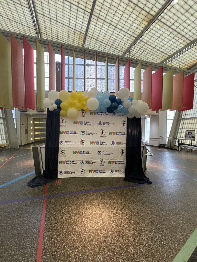 Step-and-repeat photo backdrop with NYC Public Schools logos and a balloon garland in a glass-roofed hall