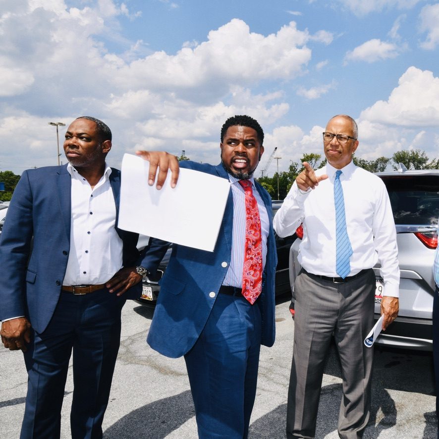 Three men in a parking lot reviewing site plans, one pointing across the property